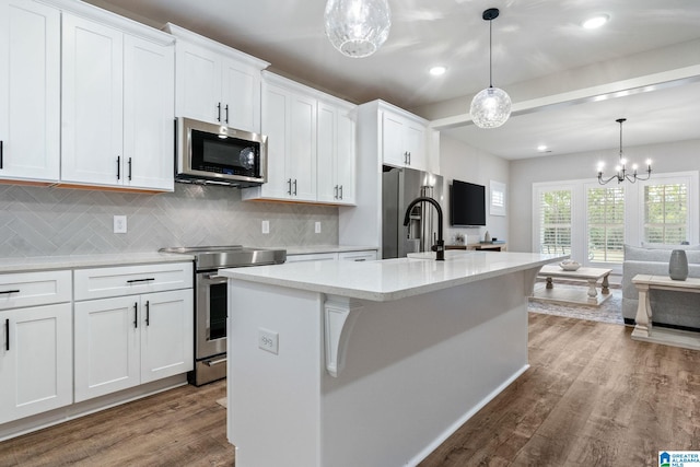 kitchen featuring hanging light fixtures, appliances with stainless steel finishes, white cabinetry, and a kitchen island with sink