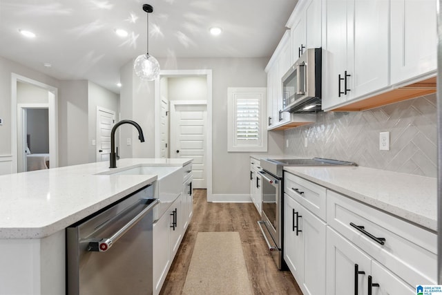 kitchen featuring tasteful backsplash, stainless steel appliances, pendant lighting, white cabinetry, and an island with sink