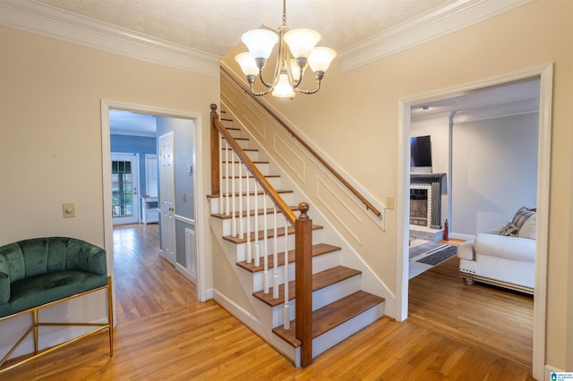 stairs featuring wood-type flooring, a chandelier, and ornamental molding