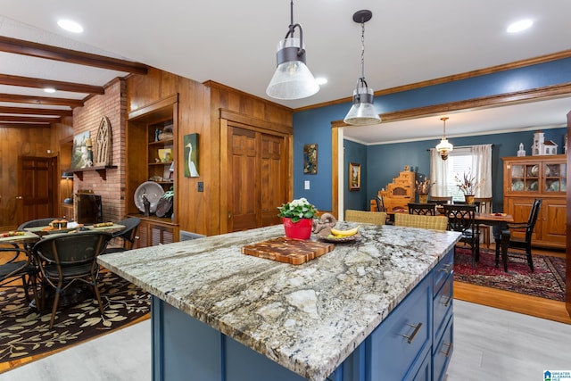 kitchen featuring beam ceiling, hanging light fixtures, blue cabinets, wood walls, and crown molding