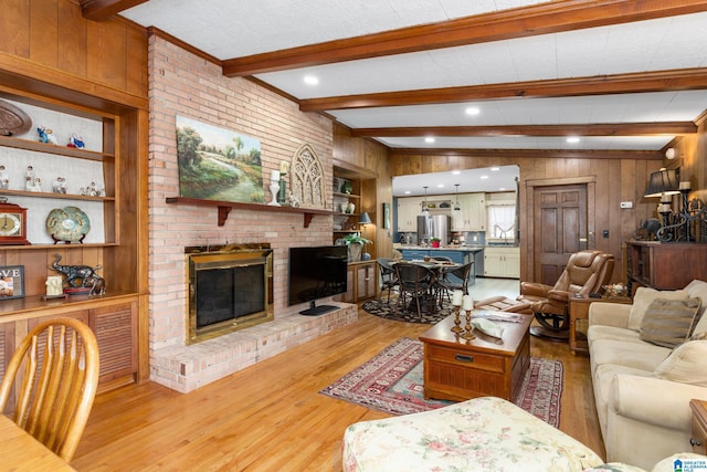 living room with beam ceiling, wood walls, a fireplace, and light hardwood / wood-style floors