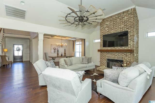 living room featuring ornate columns, an inviting chandelier, dark hardwood / wood-style floors, lofted ceiling, and a fireplace