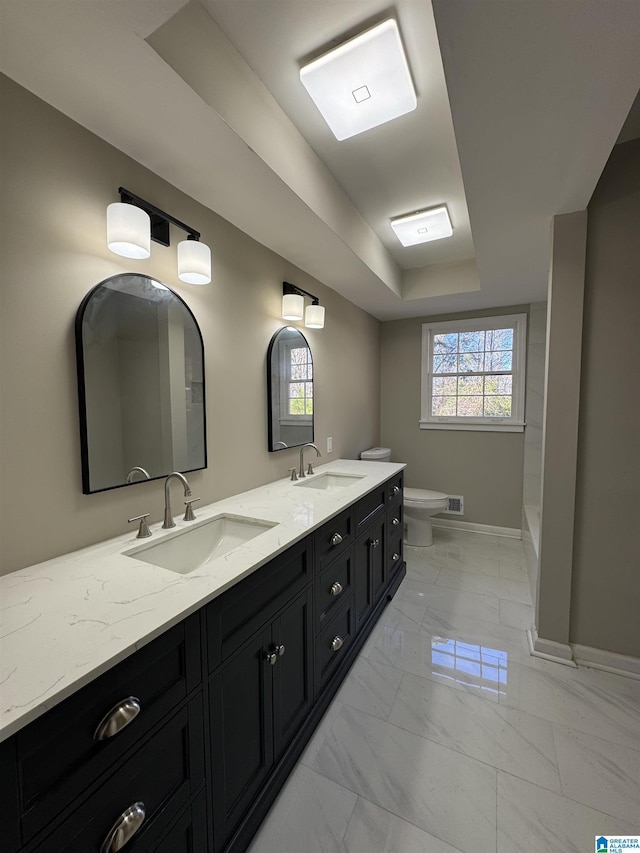 bathroom with toilet, vanity, and a tray ceiling