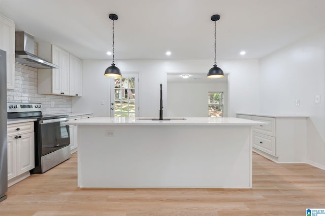 kitchen featuring white cabinets, wall chimney range hood, an island with sink, and stainless steel stove