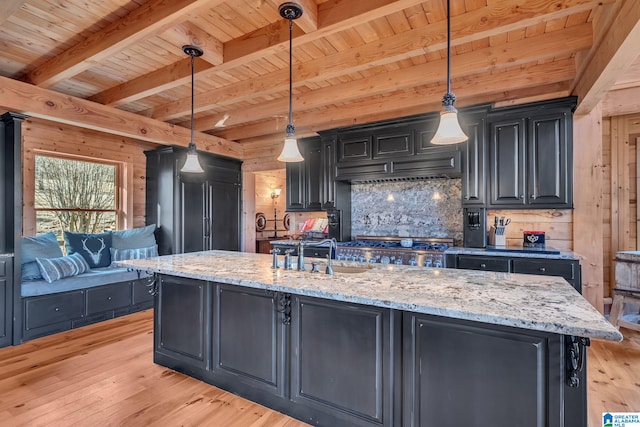 kitchen with light stone countertops, sink, an island with sink, and pendant lighting