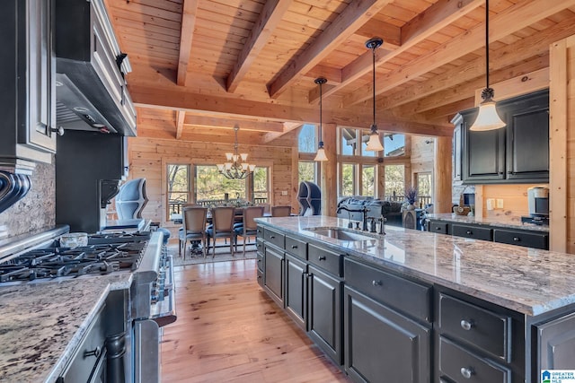 kitchen with stainless steel gas range oven, wooden ceiling, a center island with sink, beamed ceiling, and decorative light fixtures