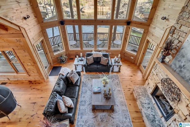 living room with light wood-type flooring, a towering ceiling, a stone fireplace, and wooden walls