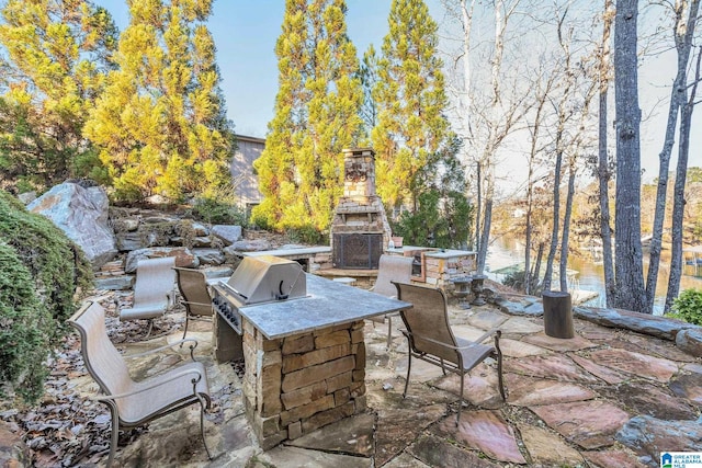 view of patio featuring a grill, a water view, exterior kitchen, and an outdoor stone fireplace