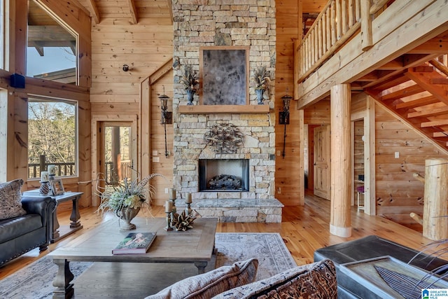 living room with a stone fireplace, beamed ceiling, high vaulted ceiling, wood walls, and hardwood / wood-style flooring