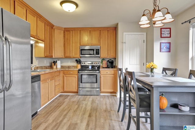 kitchen with sink, hanging light fixtures, stainless steel appliances, an inviting chandelier, and light hardwood / wood-style flooring