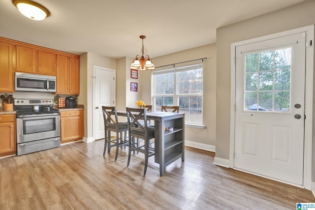 kitchen featuring light wood-type flooring, hanging light fixtures, appliances with stainless steel finishes, and a chandelier