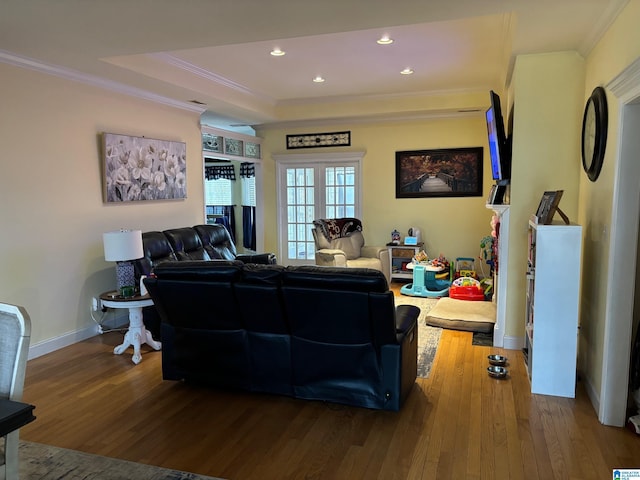 living room with wood-type flooring, a raised ceiling, and crown molding