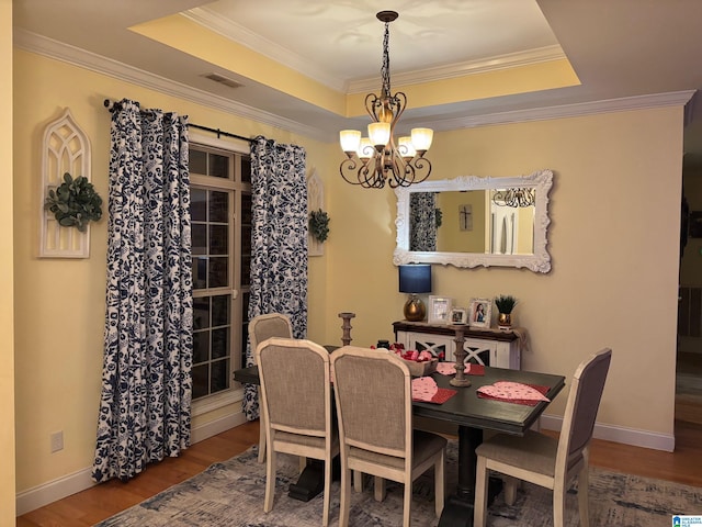 dining area featuring hardwood / wood-style flooring, an inviting chandelier, crown molding, and a raised ceiling