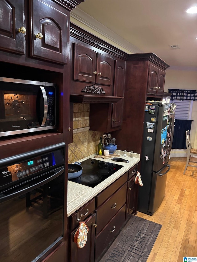 kitchen featuring decorative backsplash, dark brown cabinets, light hardwood / wood-style flooring, and black appliances