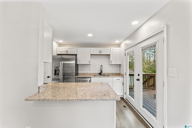 kitchen with appliances with stainless steel finishes, backsplash, white cabinetry, and light stone counters