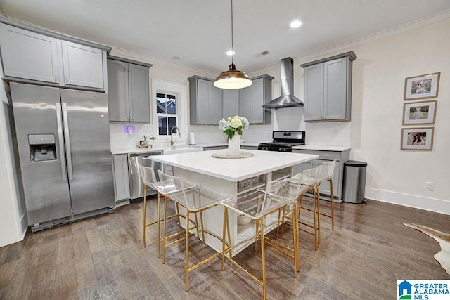 kitchen featuring gray cabinetry, dark wood-type flooring, wall chimney exhaust hood, a kitchen bar, and stainless steel appliances