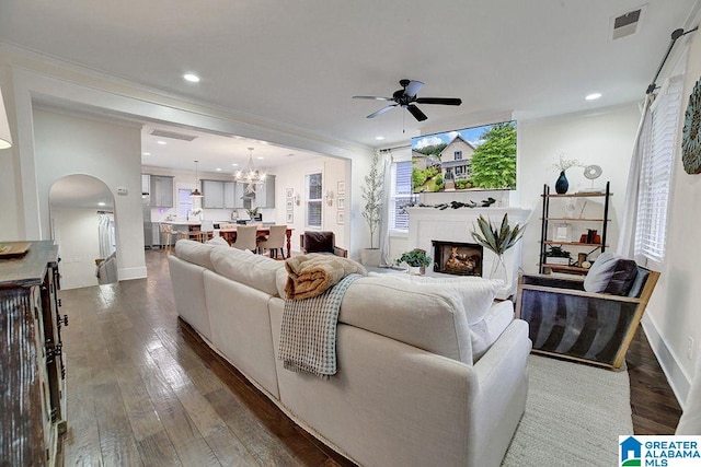 living room featuring crown molding, dark wood-type flooring, and ceiling fan with notable chandelier