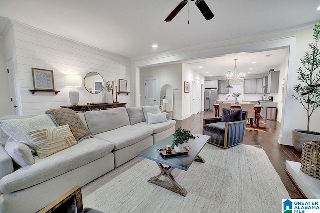 living room with wood-type flooring, ceiling fan with notable chandelier, and ornamental molding