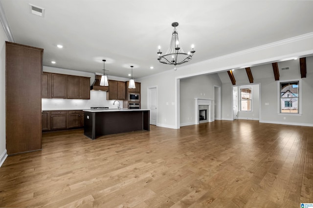 kitchen featuring decorative light fixtures, built in microwave, stainless steel oven, light hardwood / wood-style floors, and a center island with sink