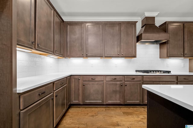 kitchen with premium range hood, backsplash, light hardwood / wood-style floors, gas stovetop, and dark brown cabinets