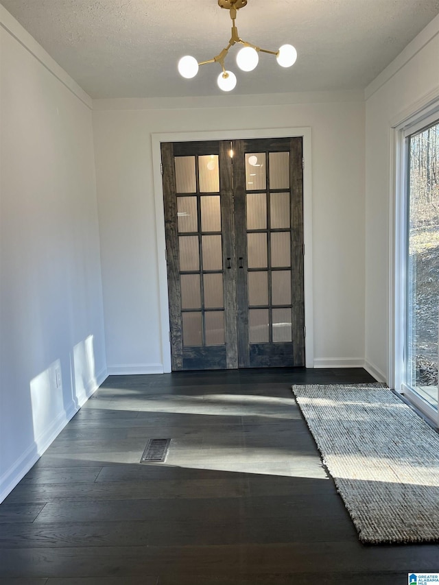 interior space with french doors, a textured ceiling, dark wood-type flooring, and a notable chandelier