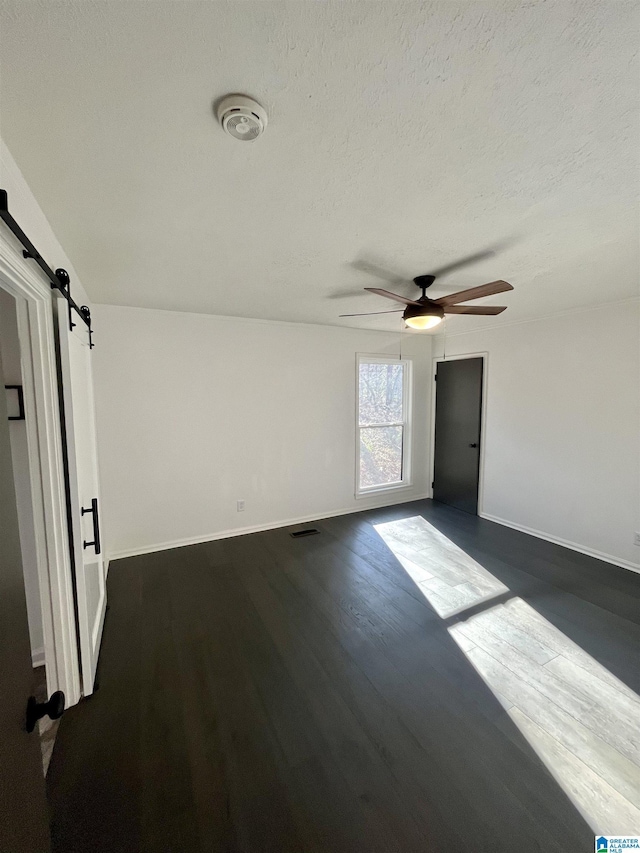 empty room with a barn door, dark hardwood / wood-style floors, and ceiling fan