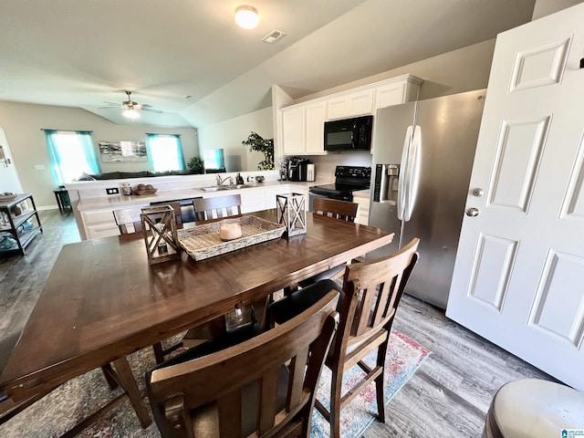 dining area featuring ceiling fan, light wood-type flooring, sink, and vaulted ceiling