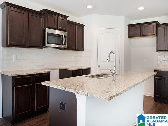 kitchen featuring sink, an island with sink, and dark wood-type flooring