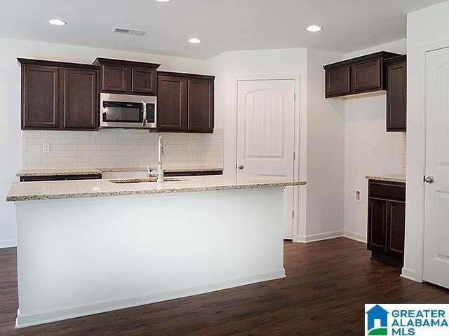 kitchen with a kitchen island with sink, sink, dark hardwood / wood-style floors, light stone countertops, and dark brown cabinetry