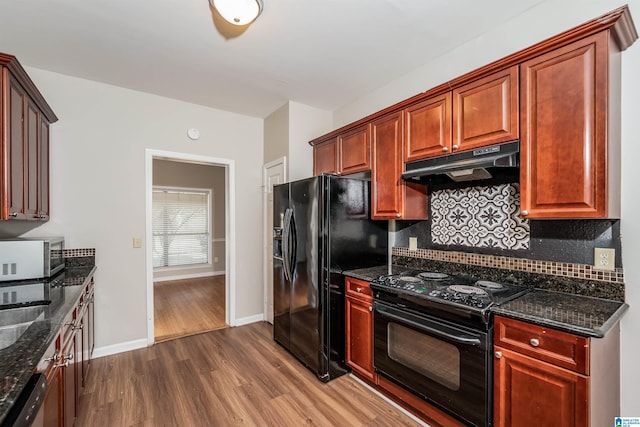 kitchen with wood-type flooring, tasteful backsplash, dark stone counters, and black appliances