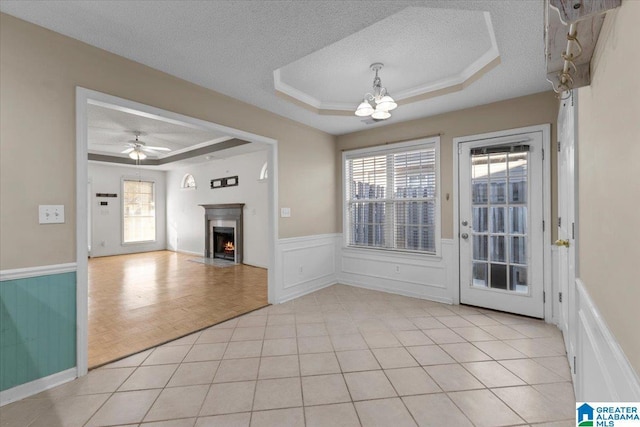 interior space featuring ceiling fan with notable chandelier, a textured ceiling, a raised ceiling, and light tile patterned flooring