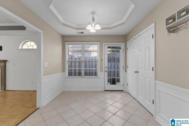 tiled foyer entrance with a chandelier, a textured ceiling, a raised ceiling, and a wealth of natural light