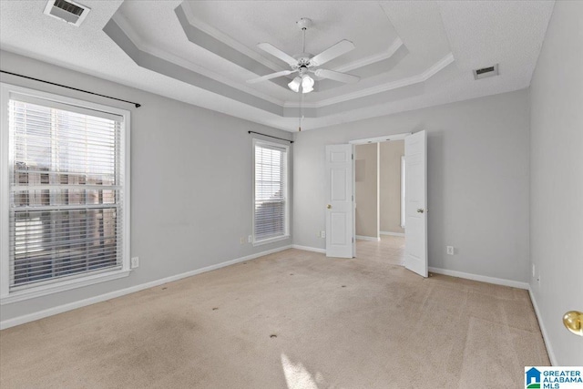 empty room with a tray ceiling, ceiling fan, crown molding, and light carpet