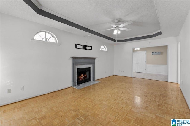 unfurnished living room featuring a raised ceiling, ceiling fan, a fireplace, a textured ceiling, and light parquet flooring