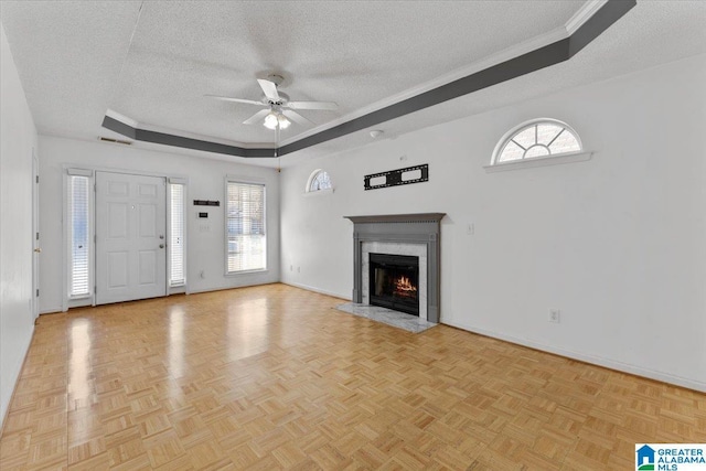 unfurnished living room with a textured ceiling, a raised ceiling, ceiling fan, and plenty of natural light