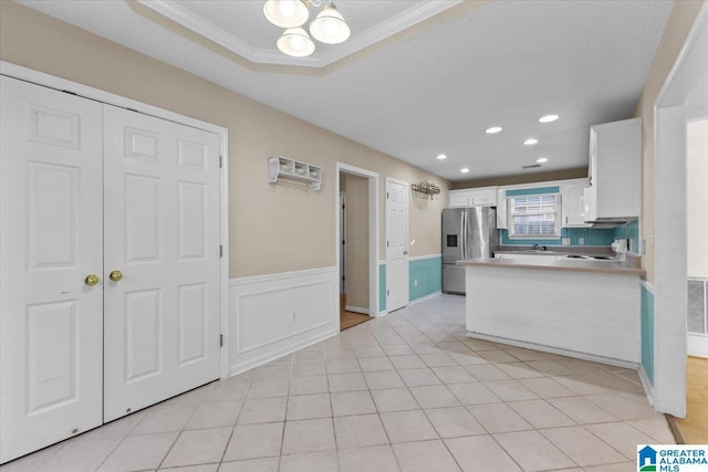 kitchen featuring white cabinets, a raised ceiling, stainless steel fridge, light tile patterned floors, and ornamental molding