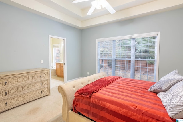 bedroom featuring a raised ceiling, ceiling fan, light colored carpet, and ensuite bathroom