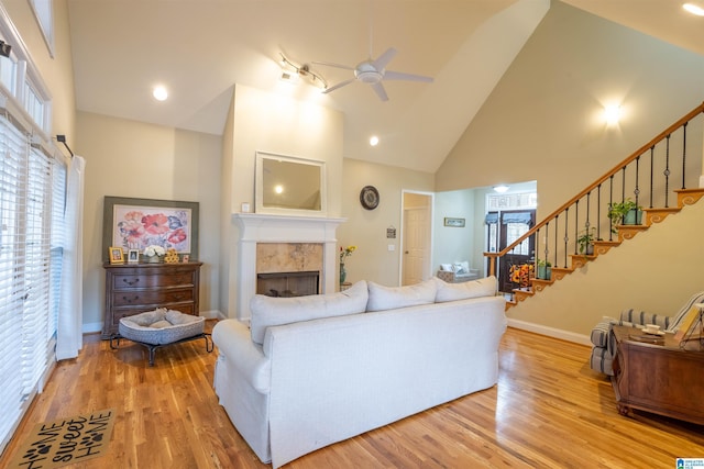 living room with ceiling fan, a wealth of natural light, light hardwood / wood-style flooring, high vaulted ceiling, and a tiled fireplace