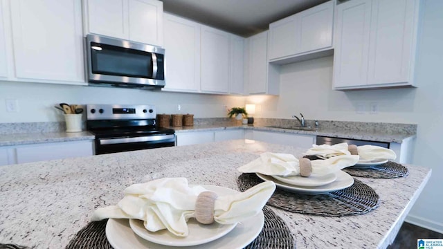 kitchen with white cabinetry, sink, stainless steel appliances, and light stone counters