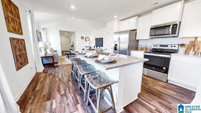 kitchen with light stone countertops, stainless steel appliances, an island with sink, a breakfast bar, and white cabinets