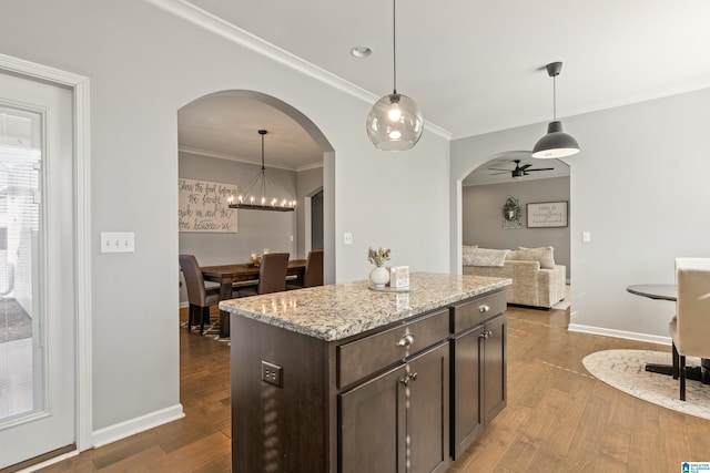 kitchen with light stone countertops, a center island, decorative light fixtures, dark brown cabinets, and ceiling fan with notable chandelier