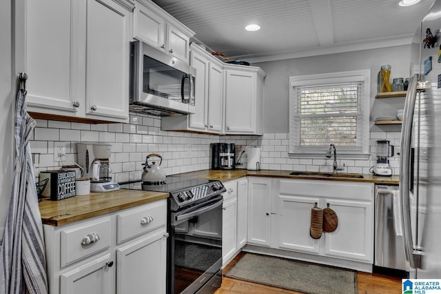 kitchen with wooden counters, white cabinets, sink, ornamental molding, and stainless steel appliances