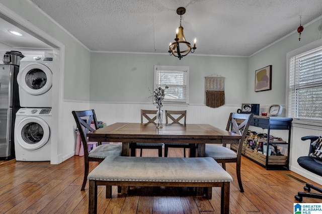 dining room featuring a textured ceiling, a notable chandelier, a healthy amount of sunlight, and stacked washer / dryer