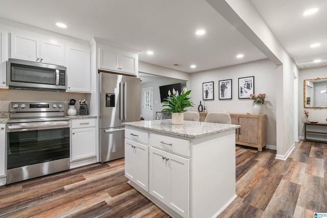 kitchen featuring light stone counters, appliances with stainless steel finishes, a kitchen island, dark hardwood / wood-style flooring, and white cabinetry