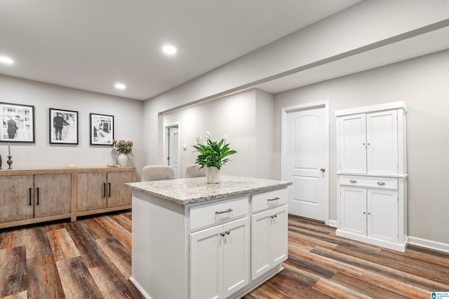 kitchen featuring dark hardwood / wood-style flooring, a kitchen island, light stone counters, and white cabinetry