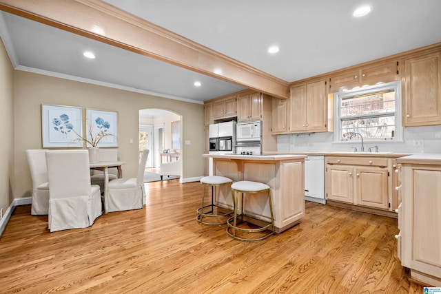 kitchen with backsplash, white appliances, light brown cabinetry, a kitchen island, and light wood-type flooring