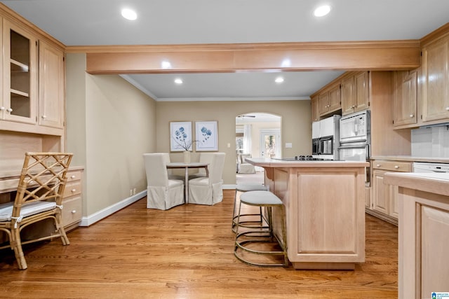 kitchen featuring light brown cabinetry, a breakfast bar, white appliances, a center island, and light hardwood / wood-style floors