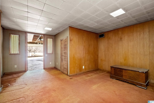 empty room featuring a paneled ceiling, wood walls, and light colored carpet