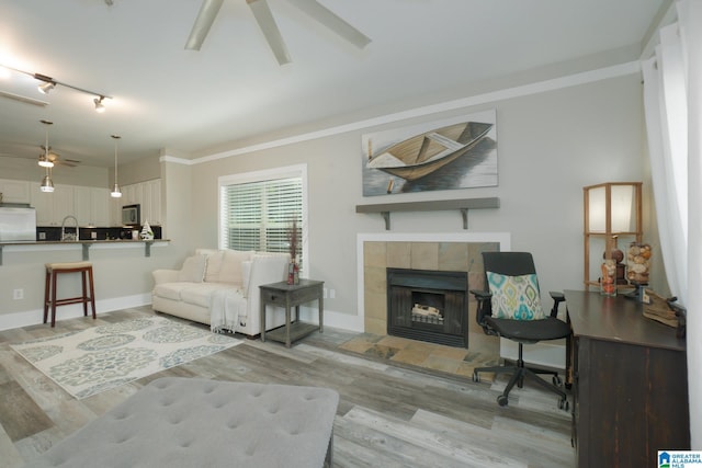 living room with a tile fireplace, rail lighting, ceiling fan, ornamental molding, and light hardwood / wood-style floors