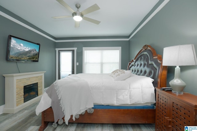 bedroom featuring hardwood / wood-style floors, ceiling fan, a stone fireplace, and crown molding